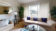 This single-floor residence offers a thoughtfully arranged layout that balances comfort and functionality across its key living spaces. The living room is an inviting retreat, featuring large windows dressed with elegant draping curtains that flood the room with natural light. Plush carpeting, a glass-top coffee table, and a generously sized sofa create a relaxed yet refined atmosphere. A decorative display cabinet and an octagonal wall mirror add character and charm to the space.

The kitchen stands out with its bold black-and-white checkered tile flooring, rich wood cabinetry, and white appliances, offering a classic aesthetic with ample storage and counter space.

The primary bedroom is a serene escape, featuring soft carpeting, natural light from a window overlooking lush greenery, and a comfortable seating area. The second bedroom is equally well-sized, with carpeted floors, a window with garden views, and convenient closet access — both rooms providing a calm, restful environment.

Two full bathrooms serve the residence, each featuring a tub-shower combination with decorative curtains, a vanity with a marble-patterned countertop, and tile flooring. Throughout the space, textured ceilings and neutral wall tones create a cohesive and welcoming ambiance.