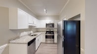 This thoughtfully renovated single-story 1-bedroom, 1-bathroom unit offers a well-designed layout with modern finishes throughout. The kitchen is a standout feature, showcasing crisp white shaker cabinetry, granite countertops, stainless steel appliances including a range, microwave, dishwasher, and refrigerator, complemented by light wood-look flooring and track lighting that brightens the space.

The open living area flows seamlessly and is anchored by a fireplace, crown molding, and a ceiling fan with light fixture. French doors lead to a sunlit nook with multiple windows offering views of surrounding greenery, filling the space with natural light. A dedicated dining area is distinguished by a classic chandelier and a decorative column accent.

The bedroom features plush carpet, a ceiling fan, a charming arched window, and built-in shelving for added storage. The full bathroom is finished with wood-look flooring, a single vanity, and a tub/shower combination. A dedicated laundry area houses a full-size washer and dryer with overhead wire shelving for added convenience, rounding out this well-appointed and move-in-ready unit.