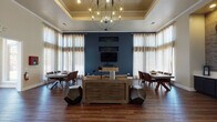 Located at 7501 S Utica Dr in Littleton, Colorado, this single-floor community clubhouse delivers an impressive blend of modern and industrial design elements. Soaring ceilings with a coffered tray detail anchor the main gathering area, where a striking globe chandelier casts warm light over rich hardwood flooring that runs throughout the space.

The main lounge area is centered around a bold deep-blue accent wall adorned with built-in display niches and a wall-mounted TV, flanked by floor-to-ceiling sheer curtains that allow abundant natural light to filter in. A rustic wood credenza and geometric sculptural accent pieces add character to the room, while two large dining tables with leather chairs on either side provide ample space for group gatherings.

A cozy seating nook features plush wingback chairs, a circular leather ottoman, and a woven area rug, creating an intimate retreat within the larger space. A pass-through window connects this area to a service counter, and a reclaimed-wood sliding barn door adds an artisan touch.

A standout wet bar area showcases dark cabinetry topped with a light quartz countertop, set against a striking mosaic stone tile feature wall displaying a cluster of decorative gear-framed mirrors, adding an eye-catching industrial-chic focal point. The overall ambiance is warm, inviting, and thoughtfully designed for both socializing and relaxation.