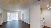This single-floor space offers a clean and functional layout with a welcoming, open feel. The main living area is finished with rich, dark hardwood flooring that contrasts neatly against the bright white walls, creating a crisp and modern aesthetic. A textured popcorn ceiling adds a classic touch overhead, while a ceiling fan provides practical comfort.

Natural light is a defining feature of the space, courtesy of a full-height sliding glass door dressed with vertical blinds. The door not only brightens the interior but also offers direct access to the outdoors. A wall-mounted heating unit is conveniently positioned nearby, ensuring year-round comfort.

The walls are finished in a clean, neutral white throughout, providing a versatile backdrop suitable for a variety of interior styles. Electrical outlets and a smoke or carbon monoxide detector are thoughtfully placed along the walls. The overall ambiance is bright, simple, and move-in ready, making it a practical and comfortable living environment. The open layout and minimal architectural detailing give the space a straightforward, functional character ideal for those seeking a clean and uncluttered living area.