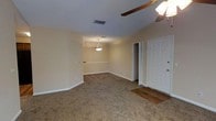 This single-floor residence offers a welcoming and functional layout highlighted by a seamless flow between the living and dining areas. The living space is finished with plush wall-to-wall carpeting in a warm neutral tone, providing a comfortable and inviting atmosphere. A ceiling fan with a light fixture anchors the living area, offering both practicality and a classic aesthetic touch. The adjacent dining area is defined by a pendant light overhead and subtle architectural detail along the upper wall, adding a touch of character to the space. Warm beige walls throughout create a cohesive, neutral palette that complements the soft carpeting and white trim work. The entryway features a paneled white door and transitions into hard flooring at the threshold, offering a durable surface at the point of entry. Vents are strategically placed throughout the ceilings to ensure consistent climate control across the living spaces. The overall ambiance is cozy and understated, making for a practical and move-in ready home with a clean, classic interior design sensibility.