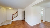 This two-story residence features a well-organized layout spread across two floors. The main level opens into a welcoming living room characterized by warm hardwood flooring, white walls, a ceiling fan, and a tiled entryway near the front door. A staircase with a wood banister and white spindles connects the floors, adding a classic architectural element to the space. The kitchen is equipped with light wood cabinetry, laminate countertops, a coil-burner electric range, a built-in range hood, and a dishwasher. Windows in the kitchen allow natural light to brighten the workspace, and a door provides direct exterior access.

The upper floor hosts all three bedrooms, each finished with neutral carpet and painted in crisp white. The bedrooms feature windows that bring in natural light, wall-mounted air conditioning units, and baseboard heating. The primary bedroom includes a closet with built-in shelving and hanging rods. A shared full bathroom on this level features a wood-toned vanity with a white countertop, a window with blinds, and light hardwood-style flooring. Baseboard heating is present throughout, contributing to a consistent and functional living environment.