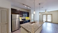 Located at 1350 N Greenville Ave in Richardson, TX, this well-appointed 2-bedroom, 2-bathroom residence offers a thoughtfully designed single-floor layout. The open-concept kitchen and living area serves as the heart of the home, showcasing granite countertops, dark espresso cabinetry, stainless steel appliances, and a large peninsula with a built-in sink and pendant lighting. Track lighting overhead adds a modern touch, while wood-style flooring flows throughout the entire unit. The living room is bright and airy, featuring a ceiling fan, neutral toned walls, and French doors that open to an outdoor patio, allowing ample natural light. The primary bedroom is a comfortable, well-sized retreat, and both bedrooms feature large windows with exterior views and wood-style flooring. The bathrooms mirror the kitchen's refined aesthetic with matching granite-topped dark vanities. A dedicated walk-in closet with built-in shelving and hanging rods provides generous storage. An additional closet offers further organizational space. A connecting hallway links the bedrooms and bathrooms with ease, contributing to the unit's efficient and functional floor plan. The overall ambiance is clean, modern, and move-in ready.