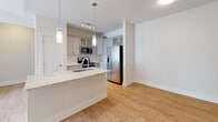 Located at 1000 Fazio Dr in Pinehurst, NC, this single-floor residence offers a thoughtfully designed layout with clean, contemporary finishes throughout. The kitchen serves as a central highlight, featuring light gray shaker-style cabinetry that extends to the ceiling, a white subway tile backsplash, light granite countertops, stainless steel appliances including a side-by-side refrigerator with water dispenser and a gas range, and a large peninsula with pendant lighting and an undermount sink — creating a seamless connection to the open living area. The living space features warm wood-look flooring, a ceiling fan, and access to natural light through a glass door. Bedrooms are carpeted and generously sized, with ceiling fans and walk-in closets featuring wire shelving systems. One bedroom includes a window with views of the surrounding exterior. The bathrooms are finished with the same light granite countertops, gray cabinetry, and wood-look flooring. One bathroom features a deep soaking tub with chrome grab bars, while another offers a wide vanity with a large mirror and bright lighting. Neutral tones, clean lines, and consistent finishes create a cohesive and comfortable atmosphere throughout the entire residence.