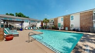 Located at 16200 Space Center Blvd in Houston, Texas, this generously sized outdoor amenity space offers a resort-style experience within a residential community. The centerpiece of the area is a large, sparkling swimming pool with crystal-clear blue water, designed with both shallow and deeper sections to accommodate a variety of uses. Clearly marked depth indicators and safety signage reflect a well-maintained and safety-conscious environment.

Surrounding the pool is a spacious concrete sun deck furnished with rows of lounge chairs and chaise lounges, providing ample space for sunbathing and relaxation. A wooden pergola adds architectural character to the deck area and offers a shaded retreat from the Texas sun. Additional seating with patio tables and market umbrellas creates casual gathering spots throughout the space.

Tropical palm trees and lush greenery are thoughtfully integrated throughout the landscape, evoking a warm, resort-like ambiance. The pool area is enclosed by black iron fencing that defines the space while maintaining an open, airy feel. The surrounding two-story buildings feature a mix of brick and light-colored siding with balconies and staircase access, framing the outdoor space with a cohesive architectural backdrop. Under the abundant Houston sunshine, this outdoor area serves as a vibrant communal hub.