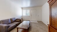 This single-floor, 2-bedroom, 1-bathroom residence offers a functional and straightforward layout designed to maximize comfort and usability. The living room greets you at the entrance, featuring neutral carpet flooring, light-toned walls, and a window with blinds that allows natural light to fill the space. A tiled entryway provides a clean transition from the front door into the carpeted living area.

The kitchen and dining area are combined into one cohesive space. The kitchen is outfitted with light wood cabinetry, dark countertops, black appliances including a refrigerator, range, and over-the-range microwave, and a peninsula with a double sink that also serves as a natural divider from the adjacent dining area. Durable wood-style flooring runs through the kitchen, transitioning to carpet in the dining space.

The hallway, finished with carpet and overhead ventilation, connects the private areas of the home. The spacious primary bedroom features carpet flooring, textured walls, and a sliding glass door that invites natural light. The second bedroom is also carpeted and offers ample wall space. The full bathroom includes wood-style flooring, a combined tub and shower with sliding glass doors, a vanity with dark countertops, and built-in open shelving for added storage.