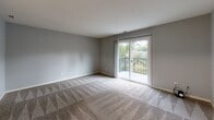 This single-floor residence offers a well-organized layout designed for comfortable everyday living. The living area is a standout space, finished with patterned carpet and bathed in natural light streaming through a sliding glass door that opens onto a private balcony with a railed enclosure overlooking greenery. The textured walls and neutral gray palette throughout lend a cohesive, modern feel to the interior.

The kitchen is well-appointed with crisp white shaker-style cabinetry extending to the ceiling, providing generous storage. Light granite countertops with subtle veining complement the white finishes, while light wood-look flooring adds warmth underfoot. A stainless steel sink completes the functional workspace.

The bedrooms are carpeted and feature soft gray walls. One bedroom includes a ceiling fan with integrated lighting and a window offering natural views, while another includes a reach-in closet with a hanging rod and direct access to additional rooms. Each bedroom provides a calm, versatile environment.

The bathroom is finished with large-format gray marble-style wall tiles surrounding a full soaking tub and shower combination, paired with chrome fixtures. The overall design of this residence balances practicality with clean, contemporary aesthetics throughout.