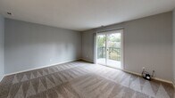 This single-floor residence offers a well-organized layout designed for comfortable everyday living. The living area is a standout space, finished with patterned carpet and bathed in natural light streaming through a sliding glass door that opens onto a private balcony with a railed enclosure overlooking greenery. The textured walls and neutral gray palette throughout lend a cohesive, modern feel to the interior.

The kitchen is well-appointed with crisp white shaker-style cabinetry extending to the ceiling, providing generous storage. Light granite countertops with subtle veining complement the white finishes, while light wood-look flooring adds warmth underfoot. A stainless steel sink completes the functional workspace.

The bedrooms are carpeted and feature soft gray walls. One bedroom includes a ceiling fan with integrated lighting and a window offering natural views, while another includes a reach-in closet with a hanging rod and direct access to additional rooms. Each bedroom provides a calm, versatile environment.

The bathroom is finished with large-format gray marble-style wall tiles surrounding a full soaking tub and shower combination, paired with chrome fixtures. The overall design of this residence balances practicality with clean, contemporary aesthetics throughout.