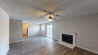 This single-floor residence offers a thoughtfully designed layout with consistent wood-look flooring and textured ceilings throughout. The spacious living room serves as the heart of the home, anchored by a white-surround fireplace and a ceiling fan with integrated lighting. Sliding glass doors open to an outdoor area, allowing natural light to fill the space. The galley-style kitchen is well-equipped with white shaker cabinetry, dark quartz countertops, subway tile backsplash, stainless steel appliances including a refrigerator, range, and over-the-range microwave, and a single-basin sink positioned beneath a window. The residence includes multiple bedrooms, each featuring ceiling fans with lighting, wood-look flooring, and windows fitted with blinds for natural light and privacy. Two bathrooms serve the home: one features a full vanity with white cabinetry and a framed mirror alongside a separate shower area, while the second includes a tub-shower combination with tile surround, a toilet, and a vanity. Clean neutral wall tones and consistent finishes throughout lend the space a cohesive, move-in-ready aesthetic.