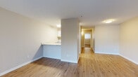 This single-story unit offers a practical and well-organized layout across a modest but efficiently utilized floor plan. The open-concept living and kitchen area forms the heart of the space, with light wood-style flooring running throughout the main areas, contributing to a clean and cohesive aesthetic. The living room is a generous, light-filled space anchored by a large sliding glass door fitted with vertical blinds, which allows abundant natural light to flow in while providing direct access to an outdoor balcony area with surrounding tree views.

The galley-style kitchen is neatly arranged with white cabinetry, white appliances including a refrigerator and electric range, a stainless steel sink, and light countertops. A pass-through counter connects the kitchen to the living area, enhancing the sense of openness.

A hallway leads from the main living area to the bedroom, which features plush carpeting, a textured ceiling, built-in closet shelving, and a window that brings in additional natural light. The bathroom includes a full tub-shower combination with grab bar, a toilet, and neutral-toned walls. Throughout the unit, neutral wall colors and consistent trim work create a clean, functional living environment.