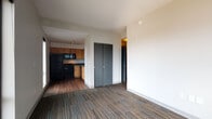 This single-floor residential unit offers a practical and modern layout designed for comfortable everyday living. The open-concept living area is finished with multi-toned striped carpeting and flows seamlessly into the kitchen, which features rich wood-toned cabinetry, dark countertops, hardwood flooring, and a full suite of black appliances including a refrigerator, gas range, microwave, and dishwasher. Ample upper and lower cabinetry provides generous storage, while a double stainless steel sink completes the functional workspace.

The bedrooms are carpeted and filled with natural light through large black-framed windows that frame views of the surrounding urban neighborhood, including tree-lined streets and neighboring buildings. Each bedroom is equipped with a wall-mounted PTAC heating and cooling unit for individual climate control.

The bathroom is finished with light tile flooring and includes a full bathtub with shower, a toilet, and convenient access to an in-unit washer. A closet with double doors in the main living area adds further storage capacity.

Throughout the unit, clean white walls, black-framed doorways, and consistent finishes create a cohesive and contemporary aesthetic suited to modern urban living.