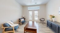 Located in Knightdale, NC, this well-appointed one-bedroom, one-bathroom unit offers a thoughtfully designed single-floor layout that maximizes functionality and comfort. The living room is bright and welcoming, featuring light wood-look flooring, a ceiling fan, and French doors with transom windows that open onto a private balcony, filling the space with natural light and outdoor views. Adjacent to the living area, the dining room is distinguished by a built-in wall of open shelving—ideal for display or storage—and an elegant pendant chandelier overhead. The kitchen is a standout feature, equipped with gray shaker-style cabinetry, granite countertops, a subway tile backsplash, stainless steel appliances including a refrigerator, range, microwave, and dishwasher, plus a peninsula for additional prep space. The generously sized primary bedroom is carpeted for comfort, features a window with natural light, and connects to a walk-in closet outfitted with wire shelving systems. The bathroom is finished with wood-look flooring, a gray vanity with granite countertops, a framed mirror, and stylish lighting. Clean neutral tones and consistent finishes throughout create a cohesive, modern aesthetic.