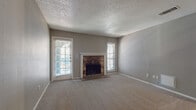 This single-story residence offers a well-organized layout across several distinct areas. The living room serves as a central gathering space, anchored by a natural stone fireplace with a white-trimmed surround and flanked by two windows fitted with horizontal blinds, allowing natural light to filter in. Neutral gray walls and wall-to-wall carpet contribute to a cohesive, understated aesthetic throughout the living areas. A textured popcorn ceiling adds a classic finish overhead, while a front entryway features durable hard-surface flooring at the threshold.

The galley-style kitchen is efficiently arranged with white cabinetry, black hardware, light countertops, a black undermount sink with a matte black faucet, and black appliances including a range and refrigerator. Wood-look flooring runs the length of the kitchen, providing a warm contrast to the white cabinetry.

The bedrooms are carpeted and each receive natural light through windows with blinds. Ceiling fans are present in the bedrooms, and one bedroom features access to a closet. Two bathrooms serve the unit: one includes wood-look flooring, a white vanity with storage cabinetry, and a tub-shower combination, while the second features a tiled tub surround and standard fixtures.