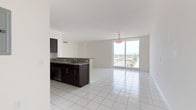 This well-appointed single-floor residence offers a clean, contemporary design throughout, unified by gleaming white tile flooring that extends across every room. The open-concept living and dining area is bathed in natural light, anchored by a dramatic floor-to-ceiling sliding glass door that leads to a balcony with expansive views of the surrounding cityscape and greenery. A stylish pendant light fixture adds a polished touch to the space.

The kitchen is thoughtfully designed with rich dark-espresso cabinetry, granite countertops, and a full suite of stainless steel appliances, including a refrigerator, range, and built-in microwave. A peninsula with a sink and additional cabinetry connects the kitchen seamlessly to the living area, making it ideal for both cooking and entertaining.

The bedrooms are bright and airy, each featuring white walls, tile flooring, and windows that bring in ample natural light, with some rooms equipped with roller shades for privacy. The bathrooms continue the unit's clean aesthetic, showcasing granite-topped vanities, white cabinetry, and a glass-enclosed shower. A second full bathroom provides additional convenience. The overall ambiance is fresh, light-filled, and move-in ready.