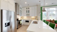 This thoughtfully designed single-floor residence combines crisp, contemporary finishes with bold pops of color to create a lively and welcoming atmosphere. The kitchen is a standout, showcasing floor-to-ceiling white shaker cabinetry, a geometric tile backsplash, quartz countertops, stainless steel appliances including a built-in microwave and range, a stainless double-basin sink, and a built-in wine rack. Pendant lighting and light wood flooring tie the space together seamlessly. The dining area opens to large windows, flooding the space with natural light, and features a striking coral accent wall that adds warmth and personality. The bedrooms are generously sized, each with wide windows offering outdoor views, ceiling fans, and light hardwood flooring. One bedroom features a bold coral accent wall and deep blue headboard, while another boasts decorative gold geometric wall art. The primary bathroom offers a dual-sink vanity with quartz countertops, a large mirror, a walk-in closet, and a separate shower. Additional bathrooms are finished with white cabinetry, tile flooring, and framed mirrors. A secondary walk-in closet features custom shelving and hanging storage. Throughout, warm neutral tones are punctuated by vibrant accents, creating a dynamic yet cohesive living environment.