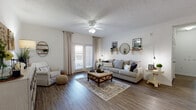 This single-floor residence showcases a cohesive farmhouse-inspired aesthetic throughout its well-appointed layout. The living room serves as the heart of the home, featuring rich hardwood-style flooring, a textured ceiling with a ceiling fan, and a set of French doors that flood the space with natural light while providing access to a private outdoor balcony. Decorative wall shelving, a round mirror, and carefully curated accents contribute to the room's warm, inviting atmosphere.

Adjacent to the living area, the dining room continues the farmhouse charm with wainscoting along the lower walls, recessed lighting, and decorative wall art. A generously sized dining table accommodates multiple guests, making it well-suited for entertaining.

The galley-style kitchen is both functional and stylish, featuring granite-look countertops, dark gray cabinetry, black appliances, and a double-basin sink — offering ample workspace and storage along both sides of the corridor layout.

The bedrooms are finished with plush carpeting and neutral tones, creating restful retreats. The primary bedroom is spacious enough to accommodate a queen-sized bed with matching nightstands. The bathroom includes a full soaking tub with a shower curtain enclosure and built-in shelving, finished in clean whites and wood-tone accents throughout.