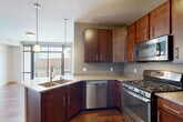 This thoughtfully designed one-bedroom, one-bathroom residence offers a efficient and modern single-floor layout. The entrance leads into a hallway with warm hardwood flooring that extends throughout the main living areas, creating a cohesive and inviting atmosphere.

The kitchen is a standout feature, outfitted with rich dark-wood cabinetry, granite countertops, and a full suite of stainless steel appliances including a gas range, microwave, dishwasher, and French door refrigerator. A peninsula with a double-basin sink and pendant lighting above adds both function and style, while floor-to-ceiling windows flood the space with natural light and provide open urban views.

The living area continues the hardwood flooring and opens directly to a private balcony through large sliding glass doors framed in black — ideal for taking in the surrounding cityscape.

The bedroom features plush carpeting, neutral walls, and a walk-in closet with built-in shelving and hanging rods, offering ample storage. The bathroom is clean and contemporary, with a white undermount sink, wood-toned vanity, framed mirror, and tiled flooring.

A connecting hallway with additional utility access ties the layout together, making this a practical and polished urban living space.