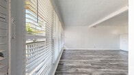 Located at 390 N Madison Ave in the heart of Pasadena, CA, this cozy one-bedroom, one-bathroom residence offers a thoughtfully laid-out floor plan across a single level. The living room is a standout feature, boasting a wall of large windows with horizontal blinds that bathe the space in abundant natural light and offer views of an outdoor balcony and surrounding greenery. Grey wood-look flooring adds a contemporary touch and flows seamlessly throughout the living area and bedroom.

The kitchen is well-appointed with white shaker-style cabinetry, granite countertops, a stainless steel range, and a double-basin sink beneath a window — creating a bright and functional cooking space. Dark hardwood-style flooring grounds the kitchen's clean aesthetic.

The bedroom features built-in white shelving and cabinetry, offering ample storage, along with a wall-mounted air conditioning unit and a ceiling with exposed beams, adding architectural character. Light wood-look flooring and a second bedroom space with sliding closet doors provide flexibility and a calm, neutral palette throughout.

The bathroom is finished with a classic black-and-white mosaic tile floor, a combined shower and tub, a granite-topped vanity, and a bright window for natural ventilation. Clean white walls throughout the entire residence create a fresh, airy ambiance ideal for comfortable living.