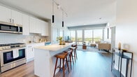 Located at 7215 N District Ave in Lincolnwood, IL, this thoughtfully designed 2-bedroom, 2-bathroom residence offers a modern open-concept layout with stylish finishes throughout. The combined kitchen and living area serves as the heart of the home, anchored by a sleek white kitchen featuring stainless steel appliances, floor-to-ceiling cabinetry, a subway tile backsplash, and a large waterfall-edge island with bar seating — ideal for both cooking and entertaining. Pendant and track lighting add a contemporary touch overhead. Rich hardwood-style flooring flows throughout the entire space. The living room is bathed in natural light, courtesy of expansive floor-to-ceiling windows and sliding glass doors that open onto a private balcony with open views of the surrounding landscape. Both bedrooms are well-proportioned, with the primary bedroom offering its own set of large windows framing bright outdoor views and access to a dedicated closet. The two bathrooms are finished with clean, neutral palettes, white vanities, lighted mirrors, and tiled walk-in showers. Two closets provide ample storage. The overall ambiance is bright, airy, and contemporary, making this a well-appointed residence in a desirable Lincolnwood location.