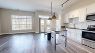 This contemporary apartment in Louisville, Kentucky, offers a blend of style and functionality. The open-concept layout maximizes space and light, with large windows providing ample natural illumination and views of the surrounding area. The living area is anchored by a sleek, built-in electric fireplace, adding both warmth and visual interest.

The kitchen is a standout feature, boasting white cabinetry, subway tile backsplash, and stainless steel appliances. A central island with a metal frame and countertop serves as both a workspace and casual dining area, illuminated by distinctive pendant lighting.

Throughout the apartment, wood-look flooring creates a cohesive and modern feel. The bathroom continues the contemporary theme with a marble-look tiled shower, dark countertops, and a large vanity mirror.

Storage is thoughtfully incorporated, with a walk-in closet featuring adjustable wire shelving. The neutral color palette of whites and soft grays provides a versatile backdrop for personal decor.

Additional amenities include a ceiling fan in the bedroom and track lighting in the kitchen, enhancing both comfort and functionality. This well-designed apartment offers a turn-key living solution in a prime Louisville location.