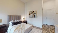 Located at 200 W Main St in New Albany, Ohio, this single-floor suite offers a refined and contemporary living experience. The bedroom is an expansive, well-appointed retreat defined by impressively tall ceilings that amplify the sense of openness throughout the space. Large, floor-to-ceiling windows flood the room with abundant natural light while framing views of the surrounding streetscape. The floors feature a striking geometric patterned tile, adding visual depth and a modern design element that anchors the room. A built-in credenza with a designated workspace provides functional versatility, complemented by curated abstract artwork displayed on the clean white walls. The en-suite bathroom continues the sophisticated aesthetic with floor-to-ceiling marble-style tile throughout, a frameless glass-enclosed walk-in shower, shiplap accent wall detailing, and sleek chrome fixtures. The overall ambiance of the suite is modern, clean, and carefully considered — balancing comfort with elevated design. The crisp white palette, high ceilings, quality finishes, and thoughtful layout combine to create a space that feels both luxurious and functional, making it an exceptional offering in the heart of New Albany.