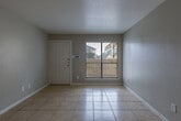 Located at 2402 Bammelwood Dr in Houston, Texas, this single-story home offers a straightforward and functional layout spread across a well-organized floor plan. The interior is finished with light-toned ceramic tile flooring throughout, providing a cohesive and easy-to-maintain surface across all living areas.

The entry leads into a bright living area featuring a front-facing window with blinds that allows natural light to fill the space. Neutral gray walls and white baseboards give the interior a clean, understated appearance. A ceiling fan with an integrated light fixture is present in one of the rooms, offering both air circulation and overhead lighting.

The kitchen is equipped with a black electric coil range, a refrigerator with top-mounted freezer, a range hood, and tile backsplash. A pass-through counter connects the kitchen to the adjacent living or dining area, enhancing the sense of openness between spaces. White cabinetry and a utility sink complete the kitchen setup.

The bathroom features a full tub and shower combination enclosed by floor-to-ceiling neutral beige tile, complemented by chrome fixtures. Additional rooms are generously sized with tile flooring and neutral wall finishes, offering flexible use as bedrooms or secondary living spaces. The overall ambiance of the home is clean, practical, and move-in ready.