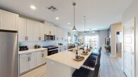 This well-designed single-floor residence offers a thoughtfully planned open-concept layout that seamlessly connects the kitchen, dining, and living areas. The kitchen is a standout feature, showcasing white shaker-style cabinetry extending to the ceiling, a herringbone tile backsplash, quartz countertops, stainless steel appliances including a gas range, microwave, refrigerator, and dishwasher, and a generously sized center island with bar seating illuminated by pendant lighting. Light wood-style flooring runs throughout the main living areas, adding warmth and continuity. The living room is bright and airy, benefiting from natural light streaming through large sliding glass doors that open to a private balcony with open views. The bedrooms feature plush carpeting, ceiling fans, and large windows that invite natural light. The primary suite connects to a well-appointed bathroom featuring a double vanity with backlit mirrors, quartz countertops, white cabinetry with matte black hardware, and direct access to a dedicated walk-in closet. A separate in-unit laundry area with side-by-side washer and dryer adds everyday convenience. The overall aesthetic is clean, contemporary, and cohesive throughout.