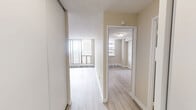 Located on the 22nd floor of 555 Sherbourne Street in Toronto, this one-bedroom, one-bathroom unit offers a well-organized layout across a single floor, comprising a living room, bedroom, kitchen, bathroom, and hallway. Light-toned hardwood flooring runs throughout, complementing the neutral warm-beige walls and white trim to create a bright, cohesive aesthetic. The living room is a standout space, featuring floor-to-ceiling sliding glass doors that open onto a private balcony, filling the room with natural light and offering sweeping views of the Toronto skyline and surrounding neighbourhood. The kitchen has been thoughtfully updated with crisp white shaker-style cabinetry, sleek brushed-nickel hardware, marble-look countertops, a white subway tile backsplash, and a stainless steel range — delivering a clean, contemporary finish. The bedroom is a comfortable retreat with a large window that brings in additional natural light and an urban view, alongside a built-in closet with sliding panel doors. A textured ceiling adds subtle character throughout the unit. The bathroom features a full soaking tub with an overhead shower, white tile surround, and clean, functional fixtures. The hallway connects all rooms efficiently, making the most of the unit's compact yet practical footprint.