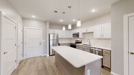 This well-appointed one-bedroom, one-bathroom unit at 2620 W Sunshine St in Springfield, Missouri offers a thoughtfully designed single-floor layout with modern finishes throughout. The open-concept kitchen serves as the heart of the home, showcasing crisp white upper cabinetry, gray lower cabinets, a classic subway tile backsplash, and a suite of stainless steel appliances including a refrigerator, electric range, microwave, and dishwasher. A generously sized kitchen island with a white quartz-style countertop provides additional prep space and is illuminated by a trio of stylish pendant lights. Light wood-look flooring runs throughout the kitchen and entry area, lending a clean, contemporary feel. The living area flows naturally from the kitchen and features soft carpeting, recessed lighting, a ceiling fan, and a door with a window that fills the room with natural light. The bedroom is a comfortable, carpeted retreat equipped with its own ceiling fan, a window with exterior views, and direct access to the full bathroom. The bathroom features tile flooring and a soaking tub/shower combination. A dedicated closet adds practical storage to complete this efficient and modern layout.