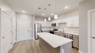 This well-appointed one-bedroom, one-bathroom unit at 2620 W Sunshine St in Springfield, Missouri offers a thoughtfully designed single-floor layout with modern finishes throughout. The open-concept kitchen serves as the heart of the home, showcasing crisp white upper cabinetry, gray lower cabinets, a classic subway tile backsplash, and a suite of stainless steel appliances including a refrigerator, electric range, microwave, and dishwasher. A generously sized kitchen island with a white quartz-style countertop provides additional prep space and is illuminated by a trio of stylish pendant lights. Light wood-look flooring runs throughout the kitchen and entry area, lending a clean, contemporary feel. The living area flows naturally from the kitchen and features soft carpeting, recessed lighting, a ceiling fan, and a door with a window that fills the room with natural light. The bedroom is a comfortable, carpeted retreat equipped with its own ceiling fan, a window with exterior views, and direct access to the full bathroom. The bathroom features tile flooring and a soaking tub/shower combination. A dedicated closet adds practical storage to complete this efficient and modern layout.