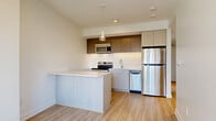 Located at 46 Flora St in Ottawa's vibrant Centretown neighbourhood, this modern 2-bedroom, 1-bathroom unit offers a well-designed single-floor layout. Light wood laminate flooring runs throughout, complementing the crisp white walls and creating a clean, cohesive aesthetic.

The kitchen is a standout feature, equipped with stainless steel appliances including a refrigerator, electric range, built-in microwave, and dishwasher. Two-toned cabinetry — light lower cabinets paired with warm taupe upper cabinets — surrounds a peninsula with a white countertop, offering additional workspace and a casual dining area. A pendant light adds a contemporary touch.

A bright hallway connects the main living areas to two well-proportioned bedrooms, each featuring the same light wood flooring and neutral walls. The primary bedroom benefits from large windows that frame views of the Ottawa skyline and surrounding neighbourhood, filling the room with natural light. The second bedroom is equally bright, with its own window and outdoor views.

The bathroom is finished with wood-grain porcelain tile in the glass-enclosed walk-in shower, providing a sleek, modern look. The unit also includes in-suite laundry, two closets, and a dedicated hallway for added functionality.