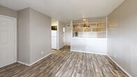 Located at 10010 Whitehurst Dr in Dallas, TX, this single-floor unit offers a practical and efficiently designed layout across a cozy footprint. The combined kitchen and living area forms the heart of the space, where wood-look laminate flooring runs throughout, providing a cohesive and clean aesthetic. A textured ceiling adds character overhead, while a ceiling fan in the living area ensures year-round comfort.

The kitchen is outfitted with dark espresso-toned cabinetry — both upper and lower — paired with light countertops that offer a functional contrast. A double-basin sink, electric coil range, built-in dishwasher, and a full-size refrigerator complete the kitchen's appliance package. An under-cabinet range hood provides added ventilation.

The living area benefits from natural light courtesy of sliding glass patio doors, creating an inviting and airy atmosphere. A distinctive open grid-style room divider visually separates the kitchen from the living space while maintaining an open feel. An additional window in a secondary nook further brightens the interior with views of surrounding greenery.

The bathroom features a dark-cabinetry vanity with a single sink, lighted mirror, and wood-look tile flooring, maintaining design continuity with the rest of the unit. A dedicated closet provides essential storage. This unit presents a straightforward, well-appointed living solution in a convenient Dallas location.