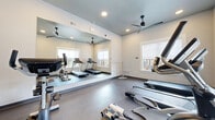 Located at 1828 Sandy Point Rd in Bryan, TX, this dedicated fitness center offers a well-appointed workout space designed to support a variety of exercise routines. The room features durable, low-maintenance flooring suited for high-traffic fitness use, complemented by neutral-toned walls and recessed lighting that create a clean, focused atmosphere.

A prominent floor-to-ceiling mirror spans one wall, effectively expanding the visual footprint of the space while allowing users to monitor their form during workouts. Ceiling fans ensure consistent air circulation throughout, contributing to a comfortable environment during exercise.

The fitness center is equipped with multiple cardio machines, including treadmills, stationary upright bikes, and elliptical trainers, as well as a rowing machine — providing a comprehensive range of cardiovascular training options. Several windows admit natural light and offer views of the surrounding outdoor areas, adding an open feel to the space.

Access is controlled via a dedicated entry door, and posted fitness center rules ensure proper use of the facility. The space is thoughtfully organized to maximize equipment capacity while maintaining clear circulation paths between machines. Overall, this fitness center delivers a practical and well-maintained environment for residents seeking convenient, on-site exercise amenities in Bryan, Texas.