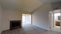 This single-floor space in Irving, Texas, presents a straightforward and functional layout highlighted by several notable architectural details. The living area serves as the central feature of the space, showcasing vaulted ceilings that lend a sense of openness and volume to the room. Soft, neutral-toned carpet covers the floor throughout, providing a warm and understated foundation that complements the light beige walls.

A tiled fireplace anchors one side of the living area, framed by dark tile work that adds a subtle contrast to the otherwise neutral palette. Adjacent to the fireplace, an opening leads into a connected area bathed in natural light, courtesy of multiple windows fitted with horizontal blinds. These windows allow ample daylight to filter through, brightening the interior and creating an airy atmosphere.

The textured ceiling adds modest architectural character throughout the space. The overall ambiance is calm and neutral, offering a clean canvas well-suited for a variety of furnishing styles. The open flow between areas and the presence of natural light make this a practical and livable single-floor space in the Irving, TX area.