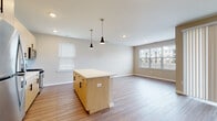 This single-floor residence showcases a contemporary design with a cohesive neutral palette and wood-look plank flooring throughout the main living areas. The open-concept layout seamlessly connects the kitchen and living space, creating a generous, airy atmosphere well-suited for both everyday living and entertaining.

The kitchen is a standout feature, outfitted with light wood cabinetry accented by matte black hardware, a white subway tile backsplash, light-toned countertops, and a full suite of stainless steel appliances including a gas range, over-the-range microwave, dishwasher, and refrigerator. A central island with pendant lighting overhead serves as a natural gathering point and provides additional prep and storage space. The living area benefits from multiple windows that invite abundant natural light and offer views of the surrounding community.

Two bathrooms are present in the unit. The primary bathroom features a glass-enclosed walk-in shower with tile surround, a single-sink vanity with light wood cabinetry, and a large mirror. The secondary bathroom offers a vanity with matching cabinetry and a toilet. The bedroom is carpeted for added comfort and includes a window for natural light, completing this well-appointed, move-in-ready residence.