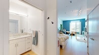 This single-floor studio in Detroit, MI offers a thoughtfully designed open-concept layout that maximizes every square foot. Light wood flooring runs throughout, creating a warm, cohesive aesthetic that ties the living, sleeping, and kitchen areas together seamlessly. A bold teal accent wall anchors the main living space, adding a vibrant focal point complemented by large sliding glass doors that flood the interior with natural light and provide views of the surrounding neighborhood.

The kitchen is well-appointed with stainless steel appliances, including a range, over-the-range microwave, and refrigerator. White cabinetry with brushed hardware pairs with granite-style countertops to deliver a clean, modern finish. A dedicated dining area with a natural wood table sits adjacent to the kitchen, creating a practical and inviting space for meals.

The bathroom features a white vanity with granite-style counters, ample storage drawers, and a well-lit mirror, maintaining the clean, modern style found throughout. Efficient use of wall hooks and towel bars adds functional detail. The overall ambiance is bright, minimal, and modern, making this Detroit studio a practical and stylish urban living space.