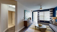 This thoughtfully designed single-floor residence showcases a modern aesthetic with bold color choices and upscale finishes throughout. The living room serves as the heart of the home, featuring a striking deep navy accent wall adorned with large-scale artwork, wood-look flooring, a ceiling fan, and direct access to an outdoor area through glass-paned French doors framed by wide striped curtains. Natural light flows generously through oversized windows.

The kitchen is a standout, outfitted with rich dark cabinetry, granite countertops, stainless steel appliances including a refrigerator, electric range, and built-in microwave, as well as a beverage cooler and an island with a deep double sink. Track lighting overhead adds a polished, functional touch.

The bedrooms offer a tranquil retreat, each with plush carpeting, ceiling fans, and bold accent walls — one in vibrant yellow and another with soft neutral tones. Walk-in closets provide generous storage. The bathroom is finished with large-format tile flooring, a soaking tub with tile surround, and dark vanity cabinetry paired with a clean white countertop.

Throughout the residence, a cohesive palette of navy, gold, and gray creates a sophisticated and energetic atmosphere.