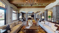 Located at 1084 W Oakland Ave in Johnson City, Tennessee, this single-floor community clubhouse is a showcase of rustic elegance and thoughtful design. The grand entrance sets the tone immediately, with a herringbone-patterned hardwood floor, towering stone columns, and a dramatic arched glass doorway that floods the foyer with natural light.

The main lounge is expansive and inviting, anchored by exposed wood ceiling beams and a striking wrought-iron chandelier overhead. Stone-clad columns with arched passageways divide the space into distinct yet open zones, creating a seamless flow between the social lounge and a game room equipped with a billiards table and entertainment area. Large arched and transom windows throughout the lounge bathe the interiors in abundant natural light and offer views of the surrounding outdoor amenities.

A dining area with rich hardwood furnishings and oversized windows overlooking the pool provides a relaxed setting for casual gatherings. A cozy meeting nook, styled with warm golden tones and built-in shelving with accent lighting, offers an intimate space for smaller group conversations. The business center is a practical, well-lit workspace featuring multiple computer stations, a printer, and natural light from adjacent windows. Throughout the clubhouse, warm wood tones, stone accents, and carefully curated décor create a welcoming and refined ambiance.