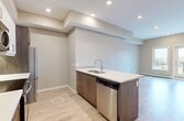 Located at 10506 121 Avenue NW in Edmonton, Alberta, this thoughtfully designed one-bedroom, one-bathroom unit offers a modern and efficient layout across a single floor. The open-concept kitchen is a standout feature, boasting a two-tone cabinetry design with rich dark lower cabinets and crisp white uppers, complemented by sleek white quartz countertops and a subway tile backsplash. A peninsula island with an integrated sink provides additional prep and casual dining space. Stainless steel appliances — including a French door refrigerator, electric range, built-in microwave, and dishwasher — complete the well-appointed kitchen. Light-toned hardwood-style flooring flows seamlessly throughout the unit, enhancing the bright, airy feel. Recessed lighting illuminates the kitchen and living areas. The bedroom is a comfortable size, featuring a window with views of the surrounding neighbourhood, a dedicated closet with rod storage, and direct access to the bathroom. The full bathroom includes a soaker tub and shower combination with tile surround. Neutral warm-grey tones on the walls throughout contribute to a clean, contemporary ambiance that feels move-in ready.