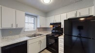 This two-story, 2-bedroom, 1.5-bathroom home offers a well-organized layout across two floors. The main level features a spacious living area with light gray walls, wood-look laminate flooring, and a fireplace framed by a diagonal wood accent wall flanked by two windows that bring in natural light. A staircase with white balusters connects the floors, and the layout provides easy flow between the living and kitchen areas. The kitchen is equipped with white cabinetry, light granite-style countertops, black appliances including a range, dishwasher, and refrigerator, along with a double-basin sink beneath a window. A conveniently located half bathroom on the main level features neutral gray walls and wood-look flooring. Upstairs, both bedrooms are carpeted and well-lit by windows with blinds. The primary bedroom features dual windows, a ceiling fan with light fixture, and ample space. The second bedroom includes a closet with built-in shelving. The full bathroom upstairs offers a marble-style vanity countertop, wood-look flooring, a window for natural ventilation, and a tiled tub-shower combination. Throughout, the home maintains a clean, neutral palette suited for a variety of interior styles.
