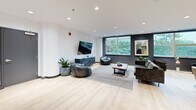 Located at 6515 Glen Erin Dr in Mississauga, Ontario, this thoughtfully designed communal lounge space offers a refined and welcoming atmosphere across a single floor. Light-toned hardwood flooring flows throughout, lending warmth and continuity to the open layout.

The space is organized into several distinct functional zones. A lounge area anchored by a dramatic floor-to-ceiling dark stone fireplace surround serves as the focal point, complemented by curved cream accent chairs, a round black coffee table, and a contemporary multi-globe chandelier overhead. Large windows in this zone frame lush greenery views, flooding the area with natural light.

A secondary lounge area features a large-screen television mounted on a dark feature wall, accompanied by casual leather seating, bean bag chairs, and a wooden coffee table set atop a textured area rug — ideal for relaxed gatherings.

The dining zone includes a striking live-edge wood table paired with upholstered chairs, positioned near the entry corridor. Decorative black circular wall accents and a framed abstract artwork contribute to the curated aesthetic throughout.

A kitchenette area finished with warm wood cabinetry and stainless steel appliances supports the space's amenity function. Recessed lighting throughout ensures consistent illumination, while the clean white walls and dark baseboards create a polished, modern contrast.