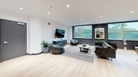Located at 6515 Glen Erin Dr in Mississauga, Ontario, this thoughtfully designed communal lounge space offers a refined and welcoming atmosphere across a single floor. Light-toned hardwood flooring flows throughout, lending warmth and continuity to the open layout.

The space is organized into several distinct functional zones. A lounge area anchored by a dramatic floor-to-ceiling dark stone fireplace surround serves as the focal point, complemented by curved cream accent chairs, a round black coffee table, and a contemporary multi-globe chandelier overhead. Large windows in this zone frame lush greenery views, flooding the area with natural light.

A secondary lounge area features a large-screen television mounted on a dark feature wall, accompanied by casual leather seating, bean bag chairs, and a wooden coffee table set atop a textured area rug — ideal for relaxed gatherings.

The dining zone includes a striking live-edge wood table paired with upholstered chairs, positioned near the entry corridor. Decorative black circular wall accents and a framed abstract artwork contribute to the curated aesthetic throughout.

A kitchenette area finished with warm wood cabinetry and stainless steel appliances supports the space's amenity function. Recessed lighting throughout ensures consistent illumination, while the clean white walls and dark baseboards create a polished, modern contrast.
