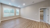 Located in Charlotte, NC, this well-appointed 2-bedroom, 2-bathroom residence offers a thoughtfully designed single-level layout finished with contemporary details throughout. The open-concept living and kitchen area serves as the heart of the home, featuring warm wood-style luxury vinyl plank flooring, neutral gray walls, and recessed lighting. The kitchen is a standout, equipped with floor-to-ceiling shaker-style cabinetry in a soft gray finish, dark quartz countertops, a central island with a built-in sink, stylish pendant lighting, and a full suite of stainless steel appliances including a French door refrigerator, range, and microwave. The spacious living room receives natural light through large windows fitted with blinds. Both bedrooms are carpeted and offer a calm, neutral palette; the primary bedroom is generously sized and connects to a luxurious en-suite bathroom featuring a double vanity with dark countertops, a soaking tub, a glass-enclosed walk-in shower, and large-format stone-look tile. The second bathroom includes a tiled tub-shower combo with marble-style surround. Two closets provide ample storage, including a walk-in closet with built-in shelving and hanging rods. A connecting hallway ties all rooms together seamlessly.