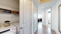 This single-floor high-rise residence is defined by its dramatic floor-to-ceiling glass walls, which frame expansive panoramic views of the city skyline and a lush urban canopy below. Natural light floods every room, reinforcing an open, airy ambiance throughout the space.

The living area is anchored by a corner configuration of oversized windows and includes access to a private balcony, making it a bright and inviting gathering space. Hardwood flooring extends through the main living and kitchen areas, adding warmth to the contemporary design.

The kitchen is outfitted with rich dark wood cabinetry, light quartz countertops, tile backsplash, stainless steel appliances including a French door refrigerator, and a window overlooking the cityscape.

Each bedroom benefits from large-format windows with sweeping views and plush carpeting. The primary suite connects to a spa-inspired bathroom featuring marble-clad floors and walls, a soaking tub, glass-enclosed shower, dual-sink vanity with wood cabinetry, and a walk-in closet with built-in shelving.

A dedicated in-unit laundry area with a front-loading Whirlpool washer and dryer, wire shelving, and panel doors completes the practical layout of this well-appointed residence.