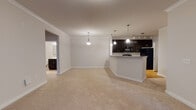 Located at 2110 Cinema Dr in Fuquay-Varina, NC, this single-floor residence offers a well-designed open-concept layout that seamlessly connects the living, dining, and kitchen areas. The living space features plush carpeting, crown molding, and pendant lighting that adds a warm, inviting ambiance. The kitchen is a standout feature, equipped with rich dark cabinetry, granite-style countertops, black appliances including a range, microwave, and refrigerator, and a large peninsula with bar seating — all illuminated by stylish pendant and track lighting. Hardwood-style flooring in the kitchen adds a practical, polished touch. The bedrooms are generously sized, each with soft carpeting, ample natural light from window blinds, and easy access to closets. Two full bathrooms mirror each other in design, featuring dark vanity cabinetry, white countertops, tiled flooring, and a tub-shower combination, offering a clean and functional aesthetic. The primary living area also includes a door with transom window that brings in additional natural light. Throughout the space, neutral tones, clean lines, and consistent finishes create a cohesive and comfortable environment suited to a variety of lifestyles.