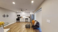 This single-story unit at 1740 Via Pacifica in Corona, California, offers a thoughtfully designed layout with a clean, contemporary aesthetic throughout. The open-concept living and kitchen area serves as the heart of the space, finished with warm wood-look luxury vinyl plank flooring that extends seamlessly across the entire floor plan. Recessed lighting and a ceiling fan keep the area bright and comfortable.

The kitchen is well-appointed with crisp white shaker-style cabinetry extending to the ceiling, offering generous storage. Light quartz countertops complement the full suite of stainless steel appliances, including a range, microwave, dishwasher, and refrigerator, alongside a deep single-basin sink. The living area accommodates seating and a dining setup, with vertical blinds on multiple windows allowing natural light to filter through.

The bedroom is separated from the main living space and features its own ceiling fan and wood-look flooring. The bathroom is notably designed with accessibility in mind, featuring a spacious roll-in shower with large-format neutral wall tile, a mosaic tile floor, grab bars, a handheld showerhead, and a linear drain — making the space both functional and inclusive.