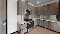 Located at 11036 Moorpark St in the Studio City neighborhood of Los Angeles, this modern single-floor residence offers a thoughtfully designed layout with clean lines and contemporary finishes. Light wood flooring flows throughout the space, complemented by crisp white walls and bold black door trim that lend a stylish, urban character.

The open living area is bright and airy, featuring track lighting and a large sliding glass door that opens to a balcony with views of the surrounding tree-lined neighborhood. The space connects seamlessly to a well-appointed kitchen outfitted with wood-grain cabinetry extending to the ceiling, white quartz countertops, a stainless steel backsplash, and a full suite of stainless steel appliances including a gas range, microwave, dishwasher, and refrigerator.

A dedicated laundry area houses a stacked washer and dryer unit, adding everyday convenience. The bedroom is a calm, sunlit retreat with a large window framing outdoor greenery. An adjacent walk-in closet features built-in shelving and organization systems. The bathroom is finished in a minimalist style, with a floating wood-tone vanity, a large backlit mirror, white quartz countertop, and a tiled soaking tub and shower combination with a built-in niche.
