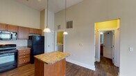 Located at 100 Village Circle Way in Durham, NC, this single-floor residence offers a thoughtfully designed layout with a blend of practical features and comfortable living spaces. The kitchen is a standout, boasting soaring vaulted ceilings that create an open, airy atmosphere. Warm honey-toned cabinetry, granite-style countertops, a central island with pendant lighting, and a full suite of black appliances — including a refrigerator, range, dishwasher, and microwave — make this kitchen both functional and inviting. Track lighting adds an additional layer of illumination overhead. The main living area continues the open feel with elevated ceilings, a ceiling fan, large windows dressed with blinds, and rich dark hardwood-style flooring that extends through the main areas of the home. The bedroom is carpeted and features a generous window with views of the surrounding greenery, bringing in natural light. The bathroom includes a tiled shower-tub combination, a granite-topped vanity, and direct access to a spacious walk-in closet with wire shelving for ample storage. A dedicated in-unit laundry area accommodates a full-size washer and dryer, adding everyday convenience to this well-appointed Durham residence.