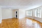 Located in Washington, DC's 20012 zip code, this one-bedroom, one-bathroom unit at 6600 Luzon Ave NW offers a well-organized layout across a single floor. The living room is a standout space, featuring a distinctive curved wall lined with large windows that flood the room with natural light and offer views of surrounding greenery. Classic parquet wood flooring runs throughout the living areas and bedroom, lending warmth and character to the entire unit. The spacious living room provides ample room for flexible furniture arrangements and connects seamlessly to the rest of the home via a central hallway. The kitchen is equipped with rich dark wood cabinetry, granite-style countertops, a gas range, and a stainless steel sink. A curved bay window in the kitchen brings in additional natural light, enhancing the functional cooking space. The bedroom is comfortably sized, featuring its own window and the same warm parquet flooring found throughout. A wall-mounted HVAC unit ensures year-round climate control. The bathroom showcases a classic black-and-white tile design with a basket-weave floor pattern, white wainscoting with black tile accents, a pedestal sink, and a window providing natural ventilation and light — a charming nod to timeless design.