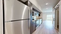 This thoughtfully designed 1-bedroom, 1-bathroom unit offers a modern aesthetic across its single floor, making efficient use of every square foot. The layout includes a living room, kitchen, bedroom, bathroom, and closet — each finished with contemporary details that create a cohesive and functional living environment.

The kitchen is a standout feature, showcasing dark wood-tone cabinetry that extends from floor to ceiling, granite countertops, and a classic white subway tile backsplash. A full suite of stainless steel appliances — including a refrigerator, range, built-in microwave, and dishwasher — lines the galley-style space. Light wood-style flooring runs through the kitchen and connects seamlessly to the main living areas, reinforcing a clean, modern feel. A stylish barn door adds a distinctive architectural touch to the hallway entrance.

The bedroom is a calm, neutral space with soft carpeting and clean white walls, offering a quiet retreat within the unit. A dedicated closet provides practical storage.

The bathroom features the same granite countertop and dark cabinetry found throughout the unit, paired with a full bathtub/shower combination and light wood-style flooring, maintaining design consistency. Recessed lighting and ceiling fans contribute to a bright, comfortable ambiance throughout the home.